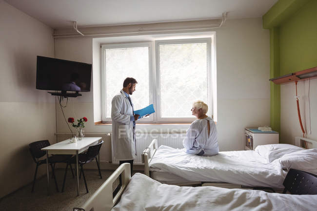 Docteur interagissant sur un rapport avec une femme âgée à l'hôpital — Photo de stock