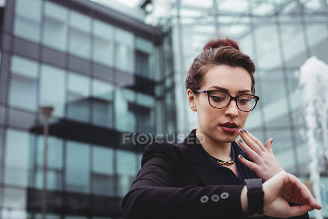 Choqué femme d'affaires vérifier le temps contre immeuble de bureaux — Photo de stock