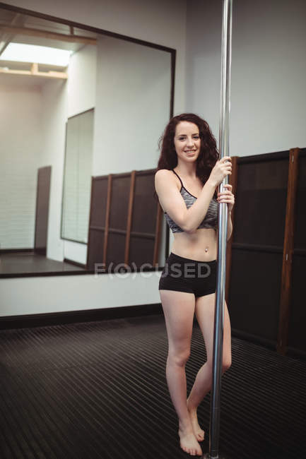Ritratto di una bella pole dancer che tiene il palo in palestra — Foto stock