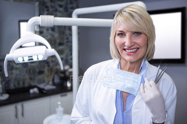 Retrato de dentista sorridente segurando ferramentas dentárias na clínica odontológica — Fotografia de Stock