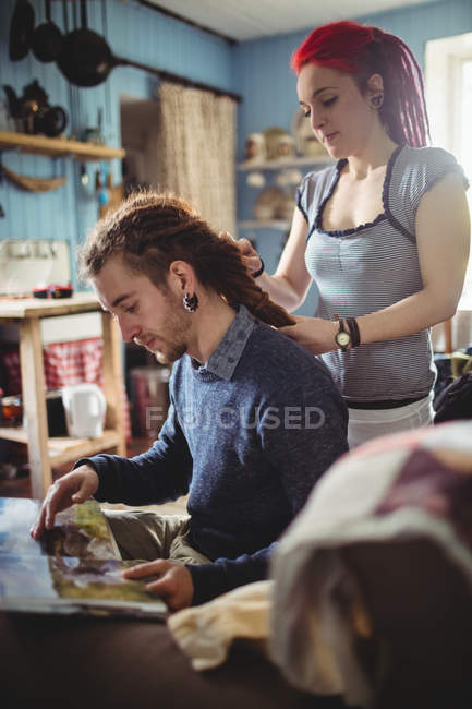 Yong woman braiding hair of hipster man at home — Stock Photo
