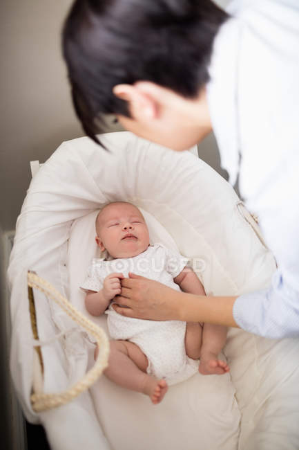 Mother looking at baby sleeping in moses basket at home — Stock Photo