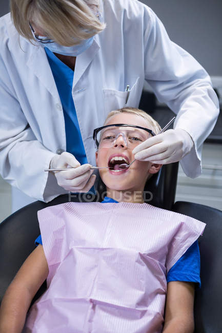 Dentista examinando um paciente jovem com ferramentas na clínica odontológica — Fotografia de Stock