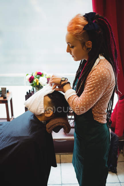 Парикмахер наносит горячее полотенце на лицо клиента в парикмахерской — стоковое фото