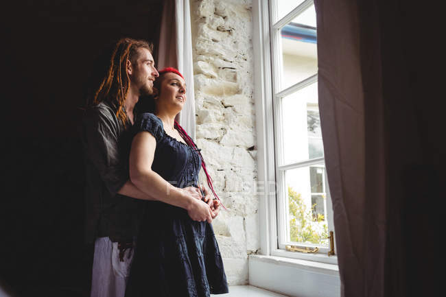 Joven pareja hipster de pie junto a la ventana en casa - foto de stock
