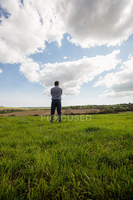 Longitud completa del hombre de pie en el campo de hierba contra el cielo nublado - foto de stock