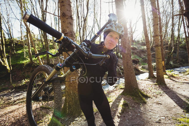 Чоловічий гірський велосипедист, що перевозить велосипед у лісі — стокове фото