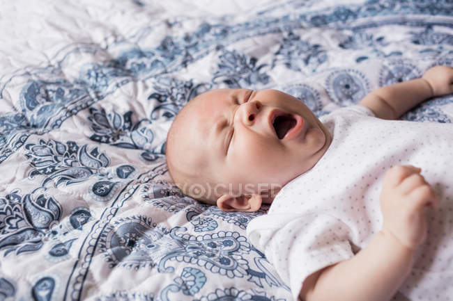 Bambino sdraiato sul letto in camera da letto e sbadigliare a casa — Foto stock