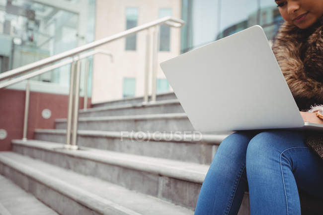 Обрезанное изображение женщины с ноутбуком, сидящей на ступеньках — стоковое фото