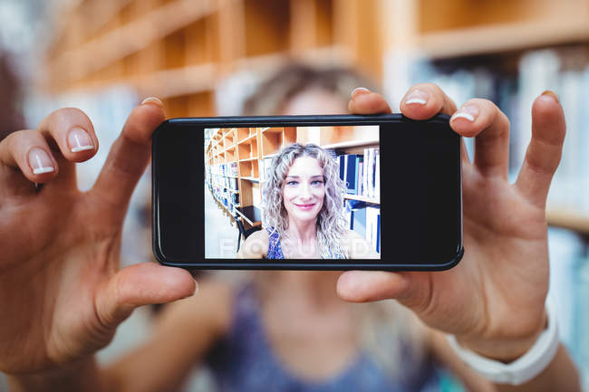 Mulher bonita tirando selfie com telefone celular na biblioteca — Fotografia de Stock