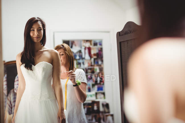 Женщина примеряет свадебное платье в студии при содействии креативного дизайнера — стоковое фото