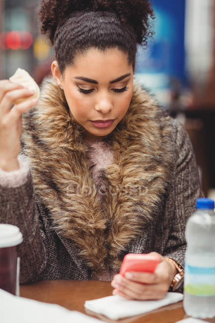 Молодая женщина использует мобильный телефон во время хлеба в ресторане — стоковое фото