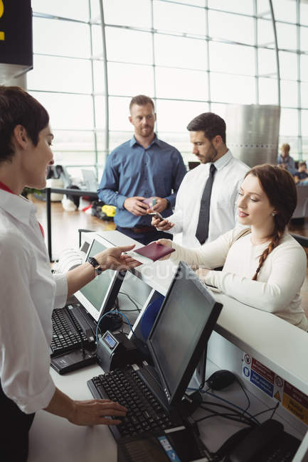 Frau gibt Flugbegleiterin am Flughafen-Check-in-Schalter ihren Reisepass — Stockfoto