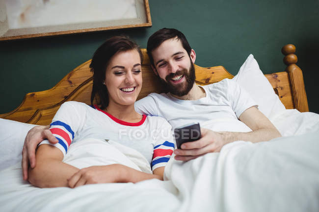 Пара використовує мобільний телефон на ліжку в спальні — стокове фото