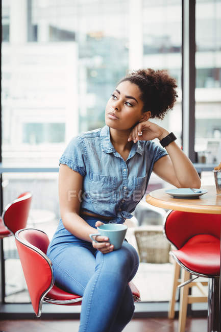 Mujer inteligente y pensativa tomando café mientras está sentada en la mesa en el restaurante - foto de stock