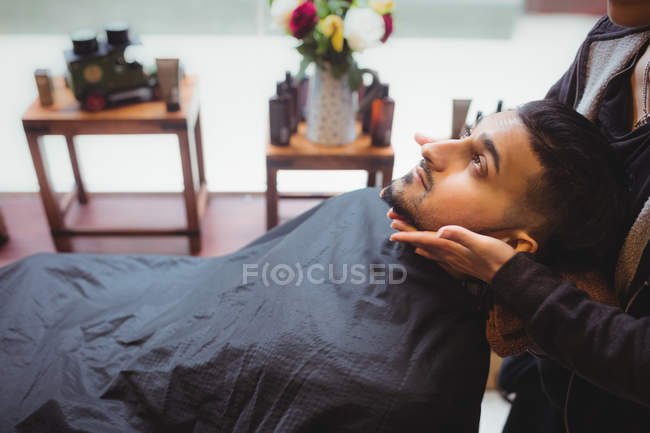 Uomo che riceve massaggio facciale da barbiere in negozio di barbiere — Foto stock