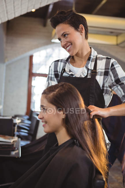 Усміхнена жінка-перукар, що працює на клієнта в перукарні — стокове фото