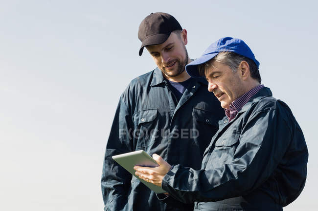 Farm workers discussing over digital tablet against clear sky — Stock Photo