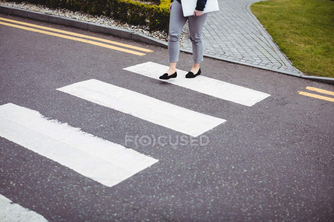 Sección baja de mujer de negocios con portátil caminando por la carretera - foto de stock