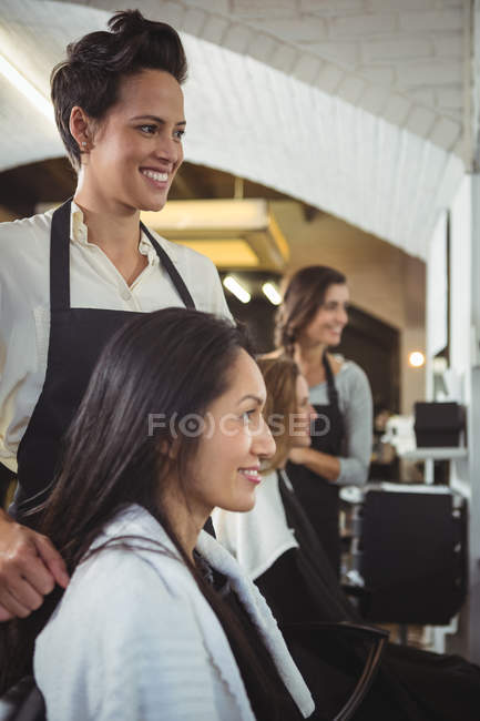 Retrato de peluqueros sonrientes trabajando en clientes en peluquería - foto de stock