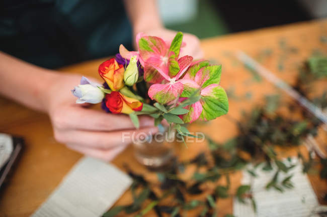 Primer plano de la floristería femenina organizando flores en una botella en su floristería - foto de stock