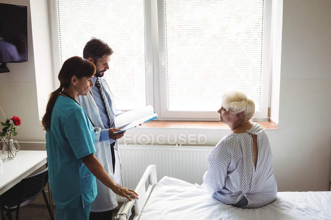 Doctors interacting over a report with senior woman in hospital — Stock Photo