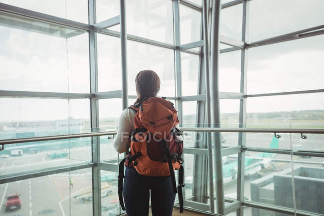 Вид ззаду жінки з багажем, який дивиться через скло в аеропорту — стокове фото