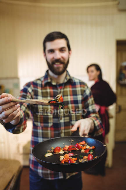 Man preparing food in kitchen at home with woman in background — Stock Photo