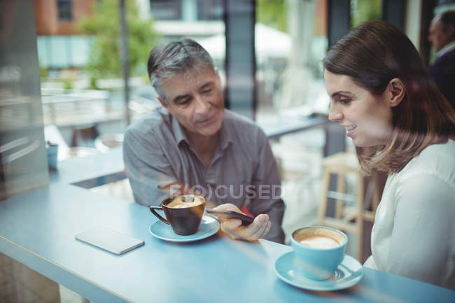 Чоловік і жінка обговорюють мобільний телефон в кафетерії — стокове фото