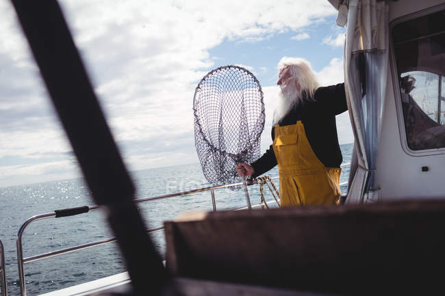Рыбак держит рыболовные сети и смотрит вдаль от лодки — стоковое фото