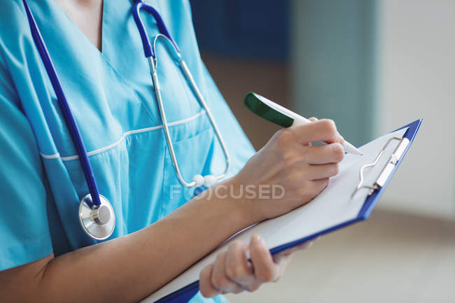 Mid section of nurse writing on clipboard at hospital — Stock Photo