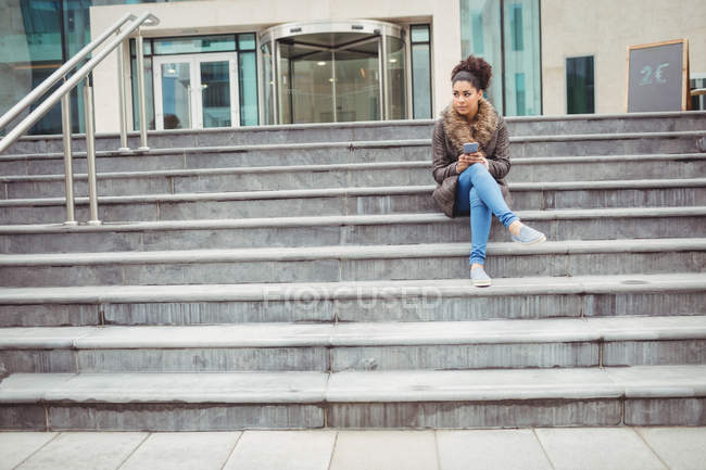 Volle Länge der Frau, die das Telefon hält, während sie auf den Stufen sitzt — Stockfoto