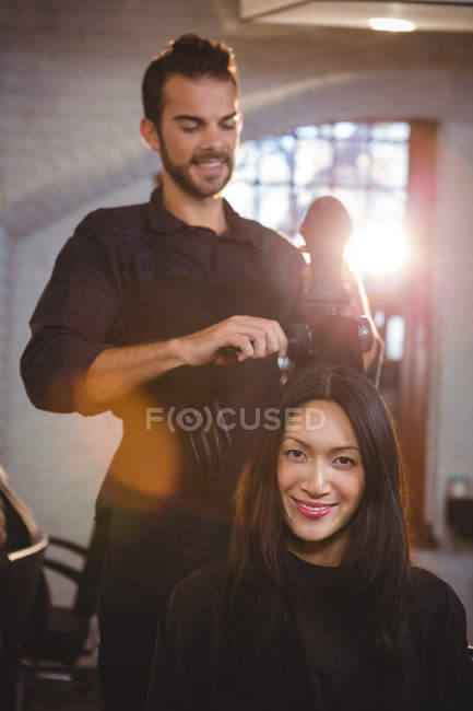 Ritratto di donna sorridente che si fa asciugare i capelli con un asciugacapelli dal parrucchiere — Foto stock