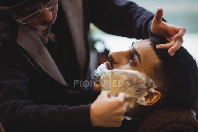 Man getting his beard shaved with shaving brush in barber shop — Stock Photo