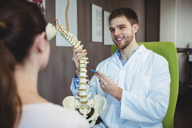 Physiothérapeute expliquant la colonne vertébrale à une patiente en clinique — Photo de stock