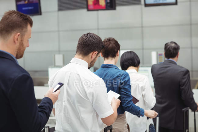 Пассажиры, стоящие в очереди у стойки регистрации с багажом внутри терминала аэропорта — стоковое фото