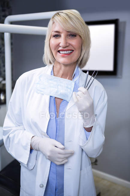 Портрет улыбающегося стоматолога, держащего в стоматологической клинике инструменты — стоковое фото