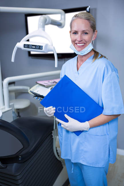 Smiling dental assistant holding clipboard in dental clinic — Stock Photo
