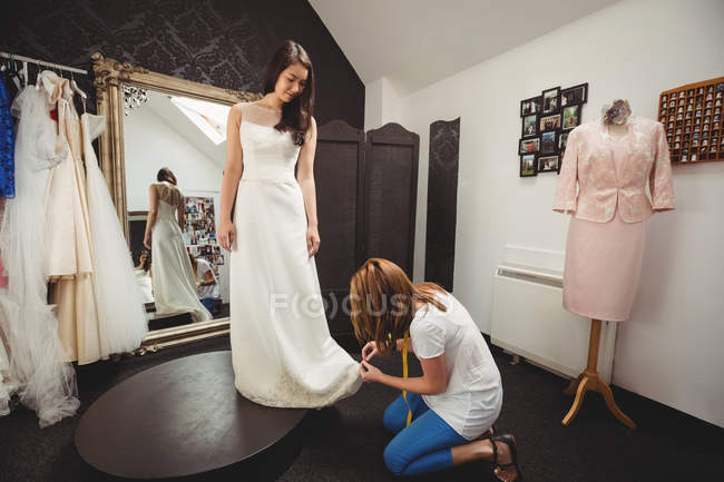 Woman trying on wedding dress in studio with assistance of creative designer — Stock Photo