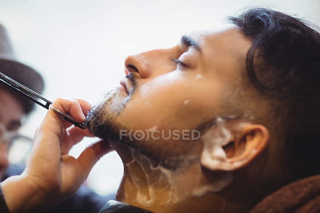 Homem com barba raspada com navalha na barbearia — Fotografia de Stock