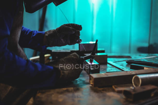 Imagen recortada de Soldador masculino trabajando en pieza de metal en taller - foto de stock
