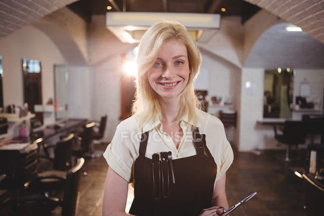 Retrato de una peluquera sonriente sosteniendo tijeras en el salón - foto de stock
