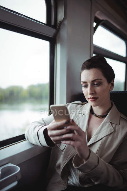 Junge Frau benutzt Handy während sie im Zug sitzt — Stockfoto
