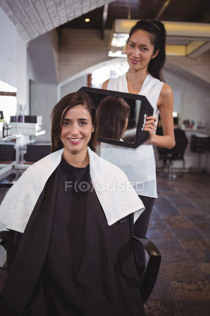 Portrait of female hairdresser showing woman her haircut in mirror at salon — Stock Photo