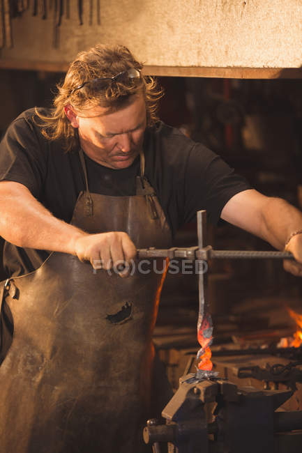 Кузнец работает на нагреваемом железном стержне в мастерской — стоковое фото