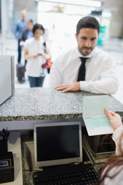 Assistente de check-in da companhia aérea que verifica o passaporte do passageiro no balcão de check-in do aeroporto — Fotografia de Stock