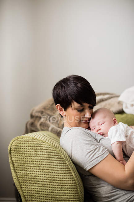 Madre che tiene il bambino mentre dorme in soggiorno a casa — Foto stock