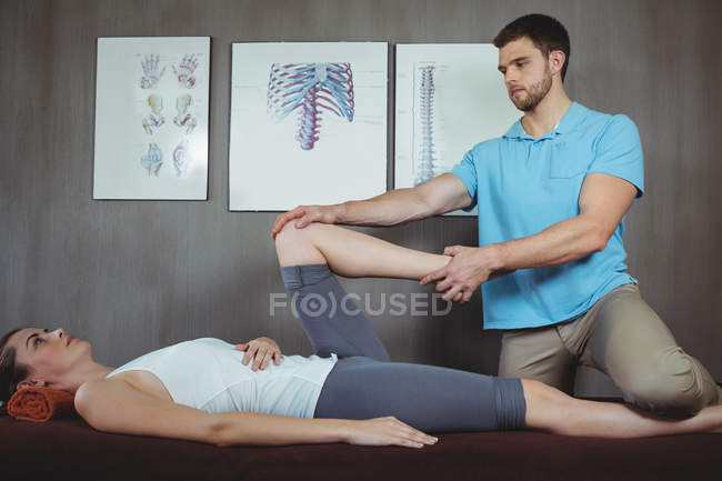 Fisioterapeuta masculino dando masaje de rodilla a paciente femenina en clínica - foto de stock