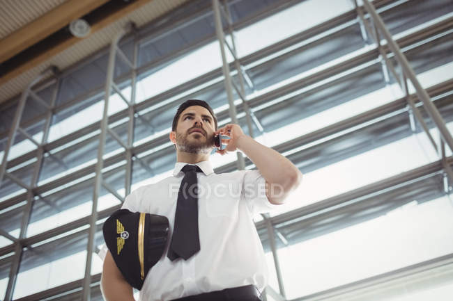 Пилот разговаривает по мобильному телефону в зоне ожидания в терминале аэропорта — стоковое фото