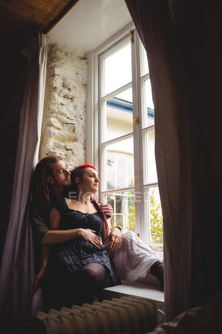 Joven pareja hipster sentada junto a la ventana en casa - foto de stock